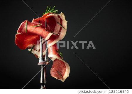 Sliced prosciutto with rosemary on a fork. Sliced prosciutto with rosemary on a fork. 122516545