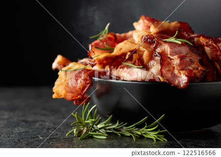 Fried bacon in a black dish with rosemary on a black background. 122516566