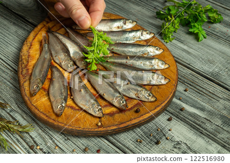 Hands gently sprinkle fresh herbs over a collection of cleaned fish laid out on a rustic wooden board, adding a touch of vibrancy and flavor to the meal, enhancing the culinary experience Hands gently sprinkle fresh herbs over a collection of cleaned fish laid out on a rustic wooden board, adding a touch of vibrancy and flavor to the meal, enhancing the culinary experience 122516980