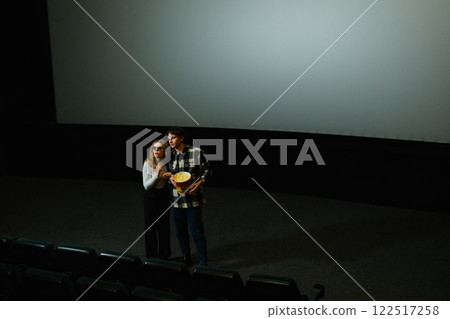Couple enjoying a movie night at a cinema with popcorn 122517258