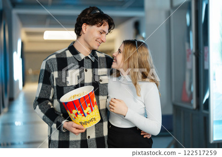 Couple enjoying popcorn while sharing a joyful moment in a cinema hallway Couple enjoying popcorn while sharing a joyful moment in a cinema hallway 122517259