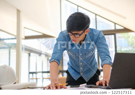 Young architect sketching house plans on a work desk in a modern office 122517311
