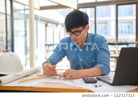 Young architect sketching house plans on a work desk in a modern office Young architect sketching house plans on a work desk in a modern office 122517313
