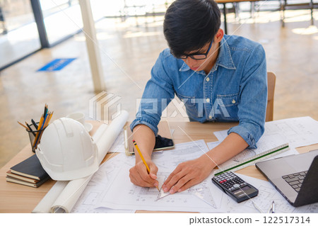 Young architect sketching house plans on a work desk in a modern office Young architect sketching house plans on a work desk in a modern office 122517314
