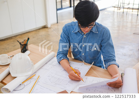 Young architect sketching house plans on a work desk in a modern office 122517333