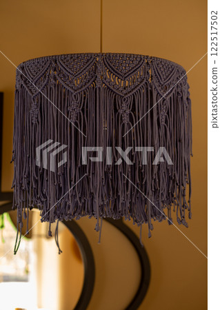 Macrame lampshade with fringes, suspended in front of a warm, background. Macrame lampshade with fringes, suspended in front of a warm, background. 122517502