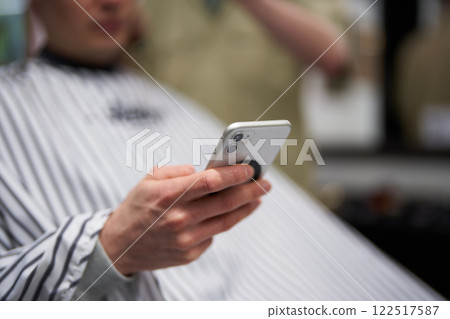 Man getting haircut while using smartphone in barbershop Man getting haircut while using smartphone in barbershop 122517587