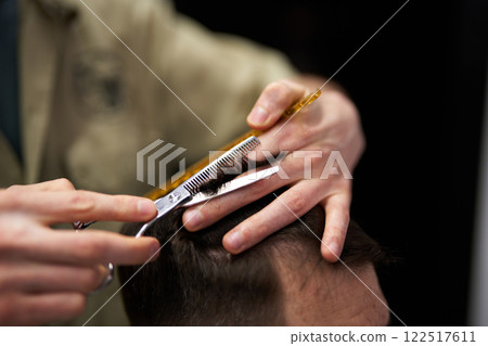 Skilled barber cutting hair with scissors and comb in modern salon 122517611