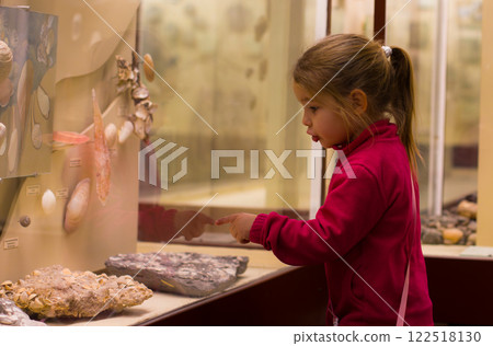A little girl indicating interesting shells and fossils for a glass demonstration in the Museum of Natural History, enjoying educational and exciting experience. The child is in the museum. 122518130