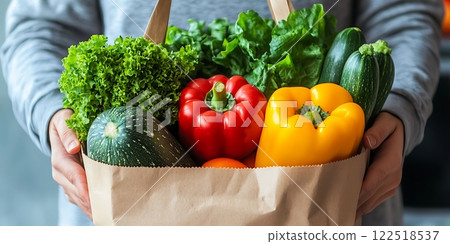 Hand holding a paper bag filled with fresh colorful vegetables including peppers and zucchini. 122518537