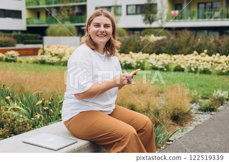 Happy woman chatting on phone and relaxing on the bench outdoors. Urban people concept. Smiling woman text messaging on smart phone at sunny day. Happy woman chatting on phone and relaxing on the bench outdoors. Urban people concept. Smiling woman text messaging on smart phone at sunny day. 122519339