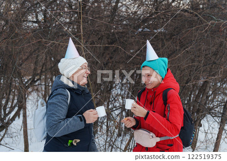 Friends savor the joy of winter in a snowy forest, wearing colorful party hats as they share warm drinks and snacks. Friends savor the joy of winter in a snowy forest, wearing colorful party hats as they share warm drinks and snacks. 122519375