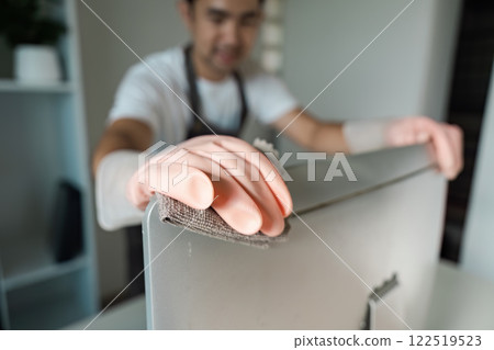 Person Cleaning Computer Monitor with Cloth and Gloves in Modern Home Office Setting 122519523
