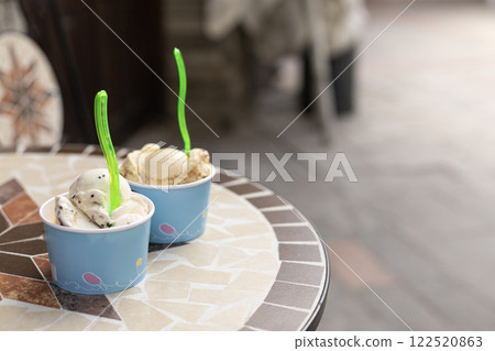 two servings of ice cream in cardboard cups on a table in a cafe outside 122520863
