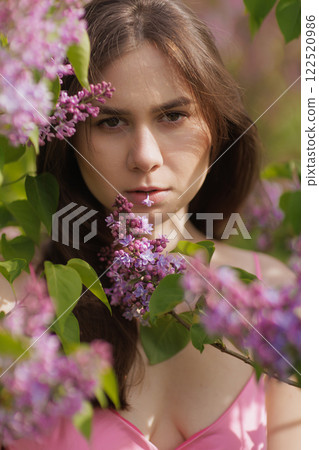 A woman in a pink dress stands among blooming lilac bushes, enjoying the spring atmosphere. relaxation and pleasure, 122520986