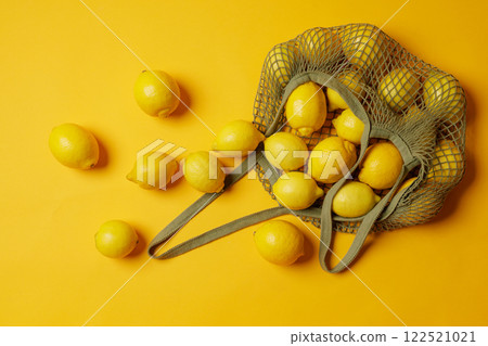 top view Mesh bag filled with fresh lemons spilling out on bright yellow background, fresh fruits, 122521021