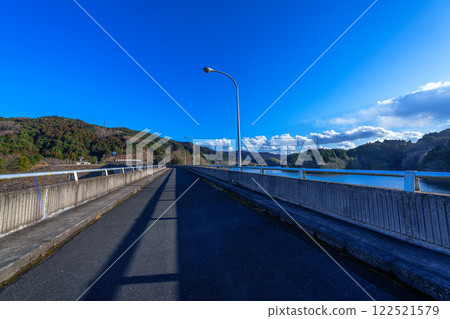 Nara City's Suijin Nunome Dam in the Yamato Plateau in the eastern part of Nara City. Midwinter scenery. A road on the dam stretching straight out to the east. Nara City's Suijin Nunome Dam in the Yamato Plateau in the eastern part of Nara City. Midwinter scenery. A road on the dam stretching straight out to the east. 122521579