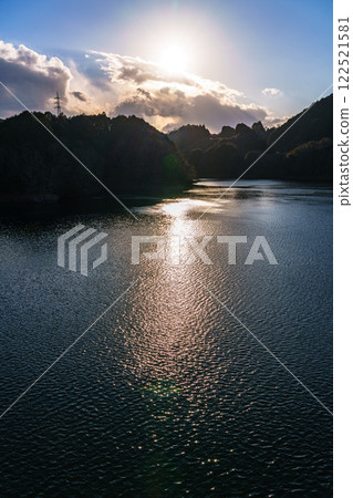 A midwinter scene at the Suijin Nunome Dam in the Yamato Plateau in eastern Nara City. The sky and lake surface turn golden as the sun sets. 122521581