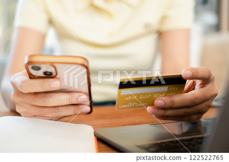 Close-up of hands holding a smartphone and credit card, illustrating online shopping and digital payment in a cozy home setting. 122522765