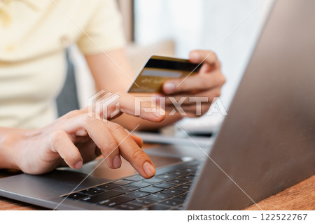 Hands holding a credit card and typing on a laptop, illustrating online shopping or e-commerce in a home environment. Hands holding a credit card and typing on a laptop, illustrating online shopping or e-commerce in a home environment. 122522767