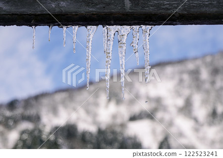 Water dripping from icicles and a snowy mountain in the background 122523241
