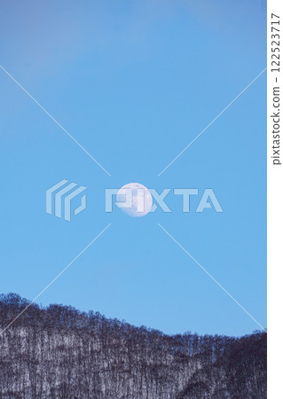 The moon shines in the depths of the snowy mountains under the blue winter sky The moon shines in the depths of the snowy mountains under the blue winter sky 122523717