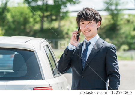 A businessman in a suit talking on a smartphone next to his car (car insurance, reservation, purchase, appraisal, trade-in) 122523860