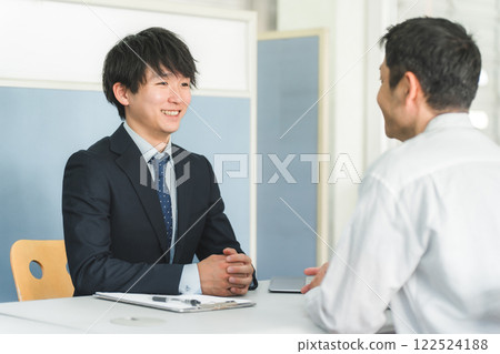 一位年輕的亞洲商人在接待處/櫃檯為男性顧客提供服務。 122524188
