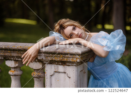 Romantic Woman in a Light Blue Gown Posing on a stone balustrade in a picturesque garden. Romantic Woman in a Light Blue Gown Posing on a stone balustrade in a picturesque garden. 122524647