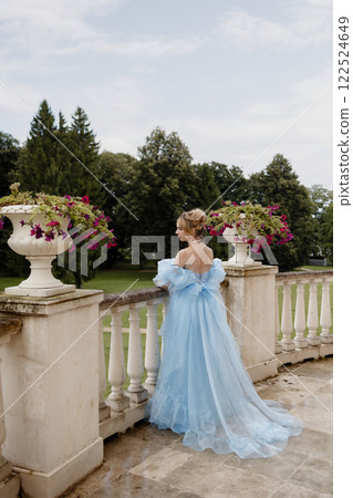 Romantic Woman in a Light Blue Gown Posing on a stone balustrade in a picturesque garden. 122524649