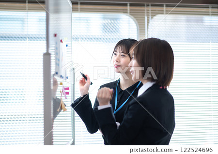 Two young businesswomen analyzing data using a whiteboard 122524696