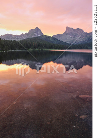 Two mountains peaks are reflected in crystal clear water of the lake at sunset 122525113