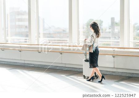 Young business woman walking with a suitcase through the lobby/corridor of an airport/train station/terminal Young business woman walking with a suitcase through the lobby/corridor of an airport/train station/terminal 122525947