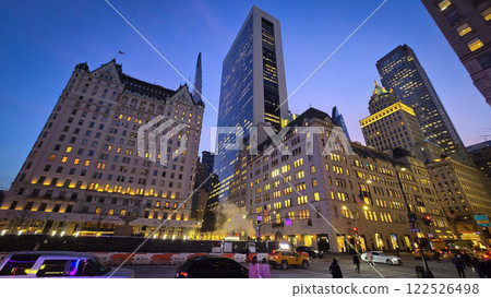 Modern look of a big metropolitan city with illuminated skyscrapers and classic architecture under a clear blue sky. Urban hustle and warm lighting create a vibrant and captivating cityscape 122526498