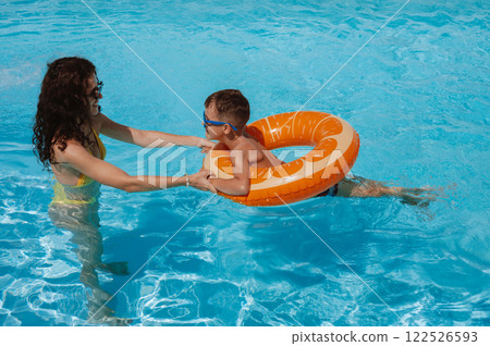 young mother teaches her child boy son to swim in swimming pool at a hotel on vacation at resort in the summer 122526593