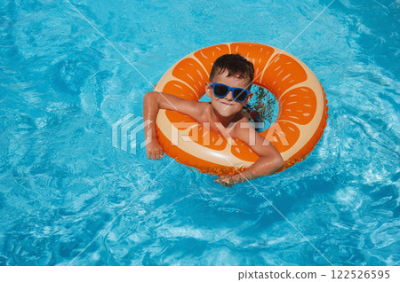 happy small child boy in inflatable circle learns to swim in the swimming pool at hotel on summer vacation 122526595