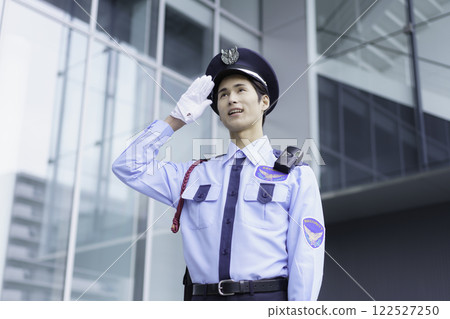 一名年輕保全在辦公大樓外站立敬禮。 一名年輕保全在辦公大樓外站立敬禮。 122527250