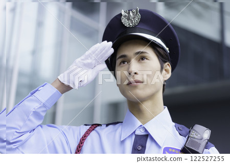 一名年輕保全在辦公大樓外站立敬禮。 一名年輕保全在辦公大樓外站立敬禮。 122527255