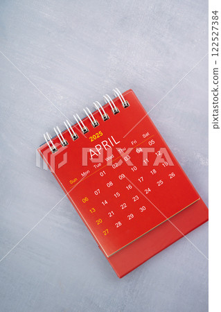 April 2025 red calendar on wooden blue background. 122527384