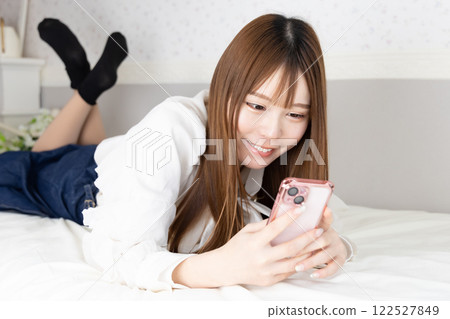 Young woman holding a smartphone on her bed 122527849