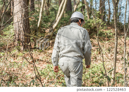 A male worker in work clothes walking through a wooded area 122528463