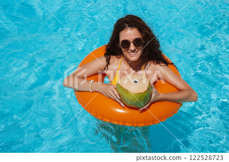 young beautiful girl in sunglasses with coconut rests in an inflatable circle in pool at a hotel on vacation at resort in summer holidays young beautiful girl in sunglasses with coconut rests in an inflatable circle in pool at a hotel on vacation at resort in summer holidays 122528723