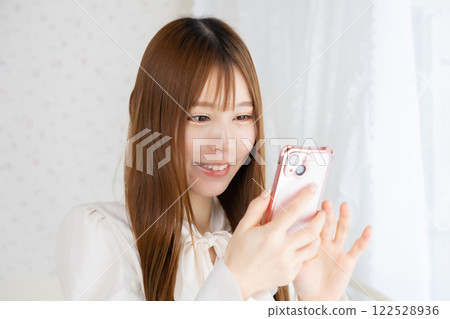Young woman holding a smartphone in her room 122528936