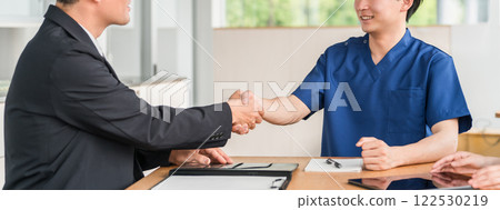 一位來自醫療設備製造商的商人和一位身穿手術服的醫生握手 122530219