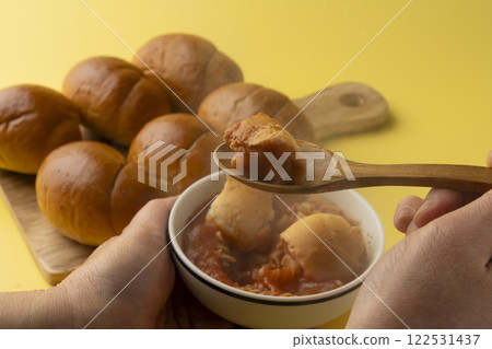 A breakfast scene with butter rolls. Dipping bread in soup. 122531437
