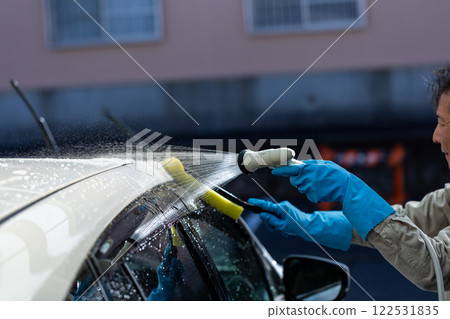 A man washing his car in his home parking lot 122531835