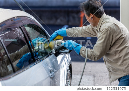 A man washing his car in his home parking lot 122531975