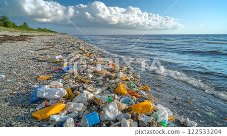 Plastic bottles, polyethylene bags and other rubbish on the seashore after storm. Garbage along the seashore against blue sea, sky and white clouds. 122533204