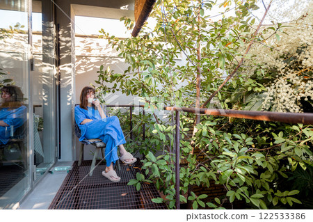 Woman Relaxing on Green Balcony with Morning Coffee Woman Relaxing on Green Balcony with Morning Coffee 122533386