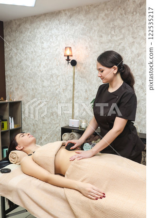 Massage of a woman's abdomen with a warm stone in a spa salon 122535217